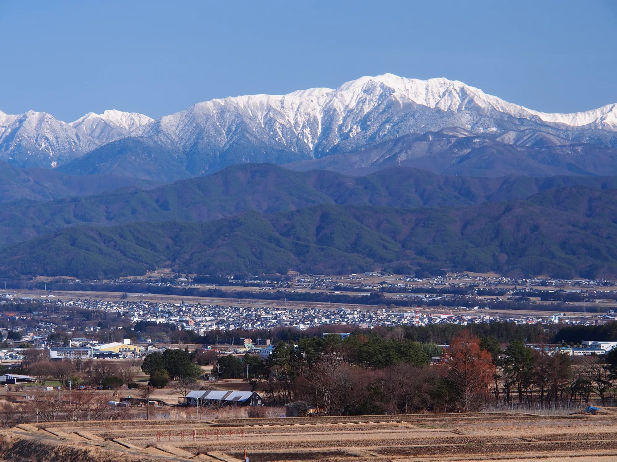 雪をかぶった信州の山並みと冬の街並み
